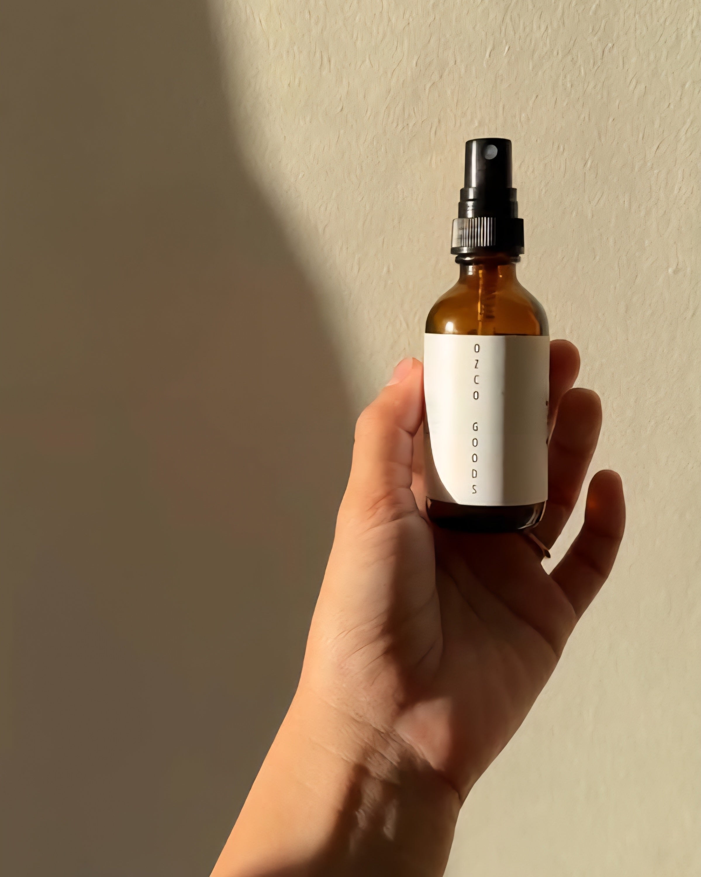 Hand holding a brown spray bottle with a white label against a beige background