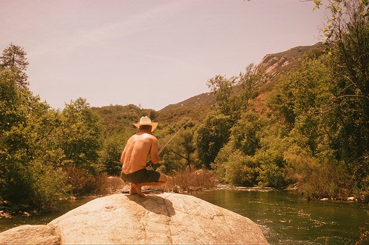 man in cowboy hat setting his fishing line at waters edge