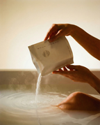 Person pouring a bag of Ozco Goods Mineral Milk Bath Soak into a bathtub with a warm glow.