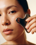 Person using a facial gua sha on their face with a neutral background