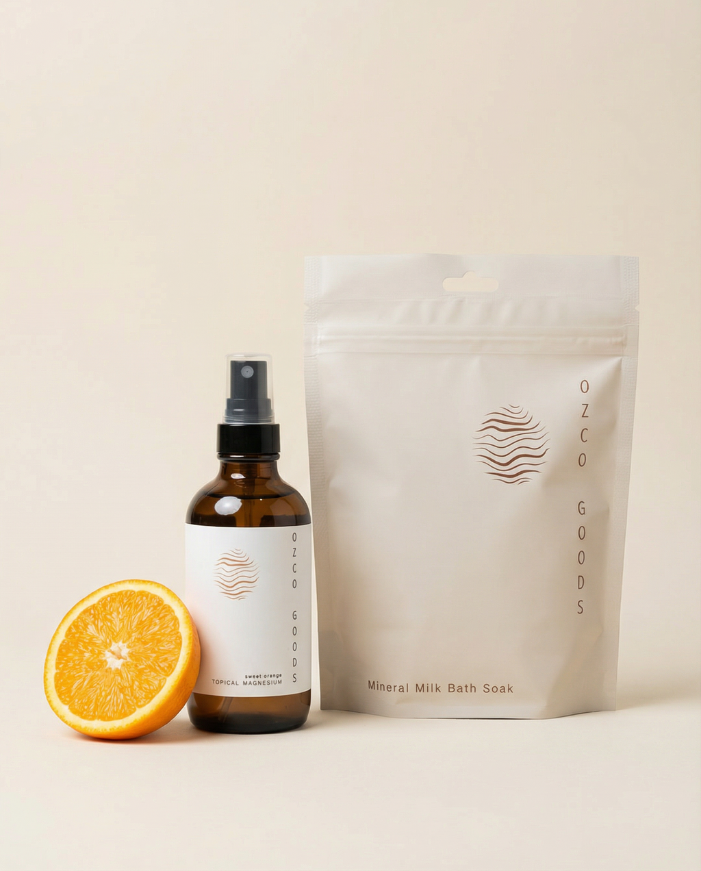 Ozco Goods Sweet Orange magnesium spray, half an orange, and a bag of bath soaks on a beige background
