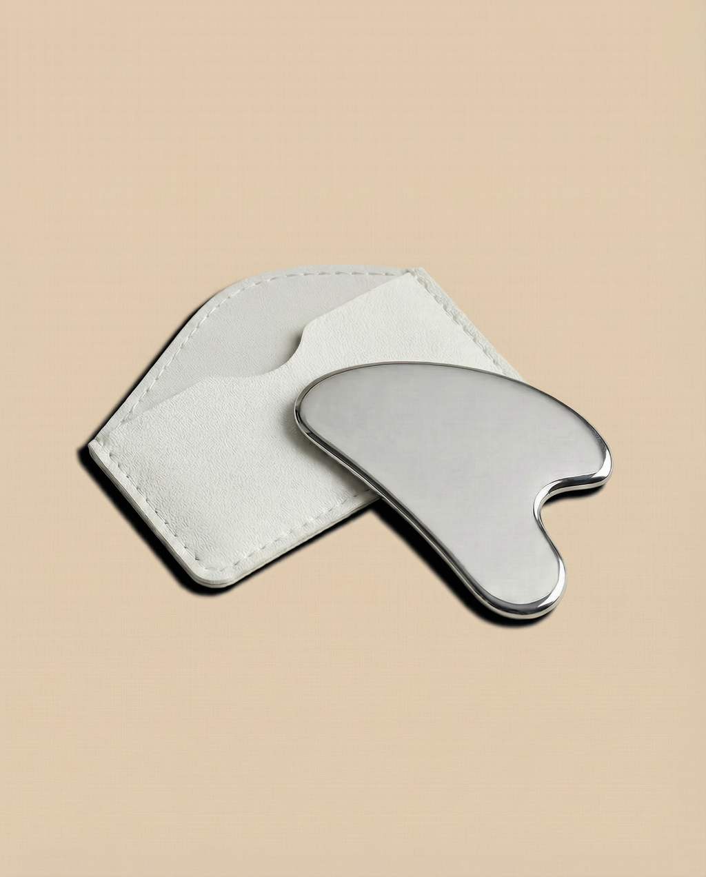 Stainless steel gua sha tool on a beige background