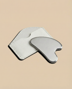Stainless steel gua sha tool on a beige background